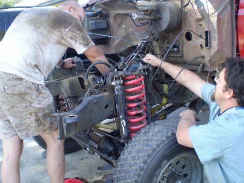 1969 Ford F-250 - Two individuals are shown working on the front suspension and engine bay of a truck, with visible red coil springs.