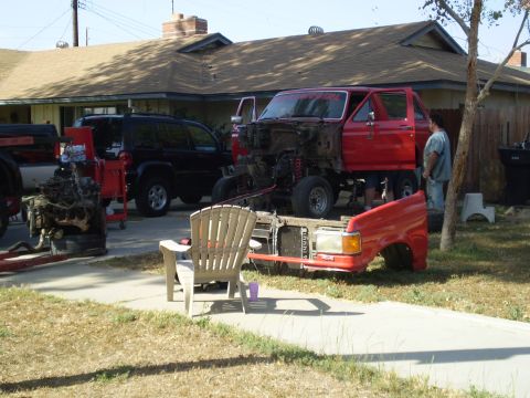 1969 Ford F-250 - A red pickup truck is disassembled in a driveway, with its front end removed and parts scattered around.