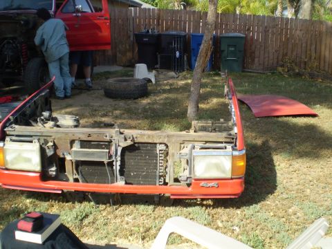 1969 Ford F-250 - Front clip of a red truck, likely from the late 1980s, is disassembled in a yard with a "4x4" badge visible.
