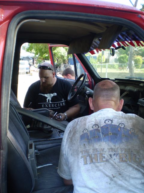 1969 Ford F-250 - Two men are inside the cab of a red truck, with a partial view of the exterior through the open door.
