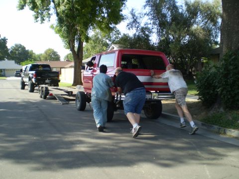 1969 Ford F-250 - Men push a red Ford Bronco while a black Ford pickup truck waits with a trailer.