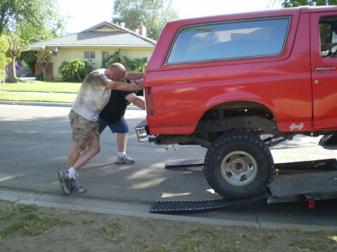 1969 Ford F-250 - Two men push a red Ford Bronco onto a trailer, with "4x4" visible on the rear quarter panel.