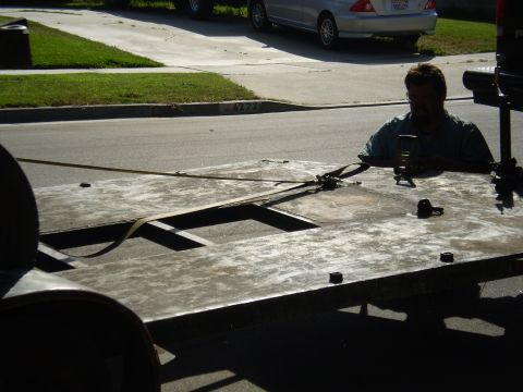 1969 Ford F-250 - A man secures a trailer bed with straps, while a silver sedan is parked on the street.