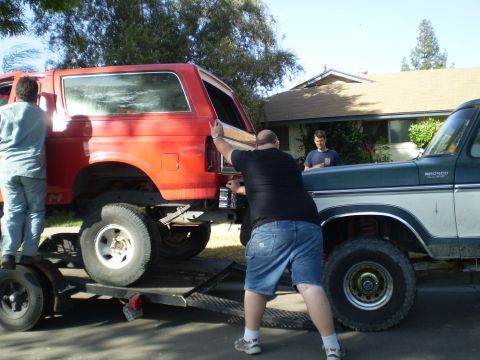 1969 Ford F-250 - A red Ford Bronco is loaded onto a trailer, with a green and white Ford F-150 pickup truck beside it.