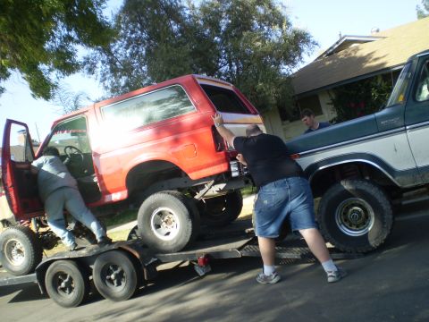 1969 Ford F-250 - Loading a red Ford Bronco onto a trailer, assisted by a green Ford pickup truck.