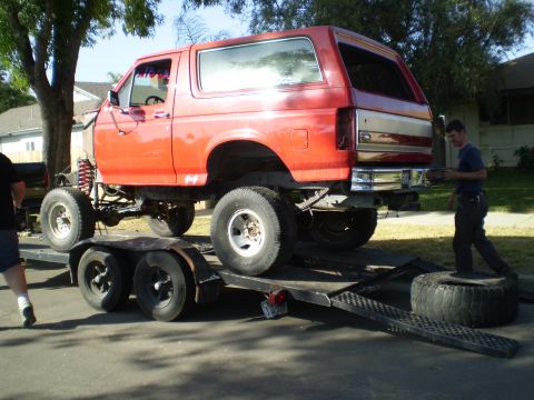 1969 Ford F-250 - A red Ford Bronco is being loaded onto a trailer, showing its lifted suspension and large off-road tires.