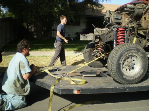 1969 Ford F-250 - Two men secure a truck chassis onto a trailer for transport.