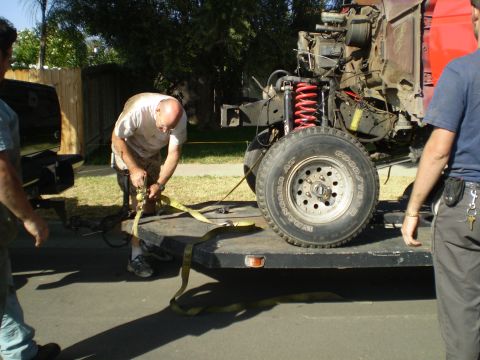 1969 Ford F-250 - Men securing a truck chassis onto a trailer for transport.