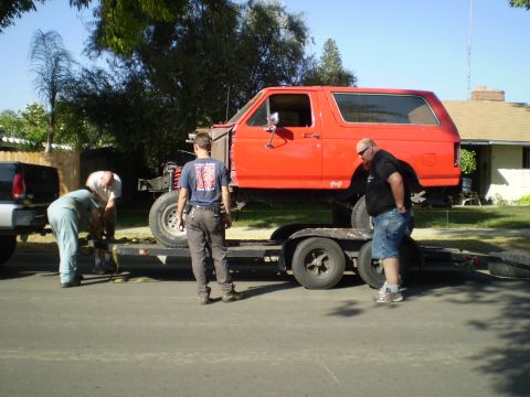 1969 Ford F-250 - Two men are securing a red SUV body to a trailer, with a pickup truck hitched to the front.
