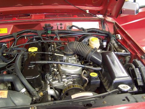 1991 Jeep Comanche - The engine bay of a red 1991 Jeep Comanche shows its internal components and wiring.