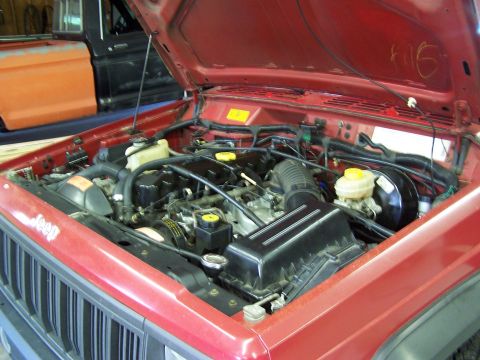 1991 Jeep Comanche - The engine compartment of a red Jeep Comanche is shown with the hood raised, revealing the engine and various components.