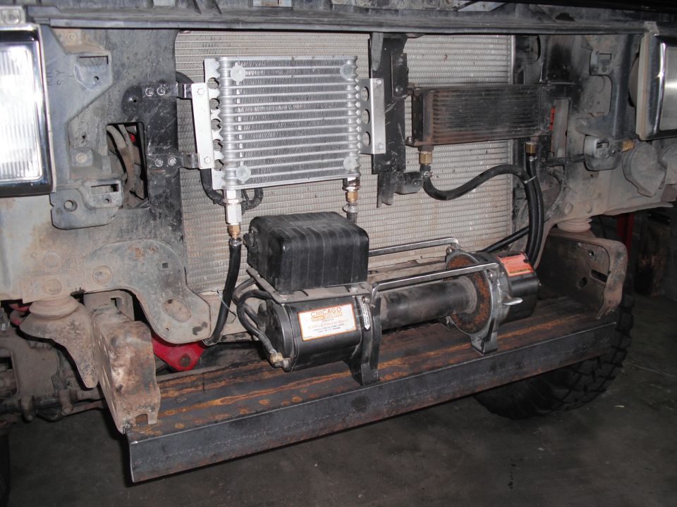 Winch and transmission cooler mounted on a vehicle's front frame. Visible text on winch label
