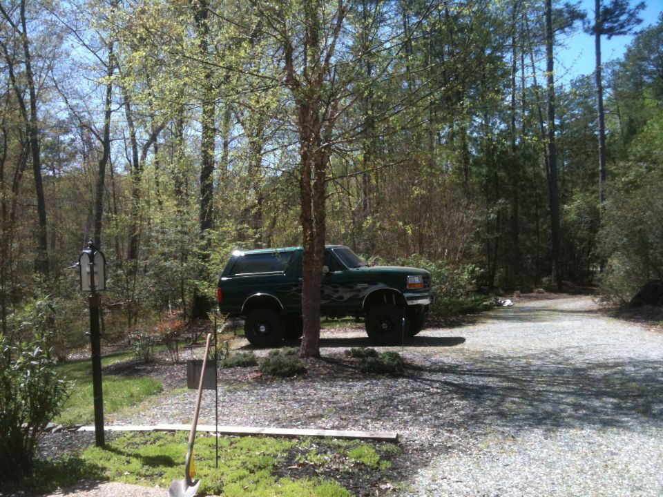 Green Ford Bronco parked on gravel drive, surrounded by trees