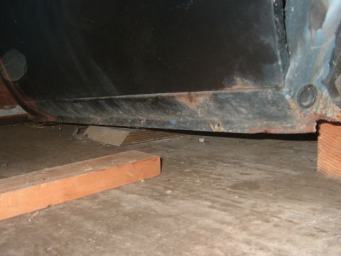 1985 Chevrolet C/K Pickup - The underside of a vehicle's body panel, showing signs of rust and resting on wooden supports.