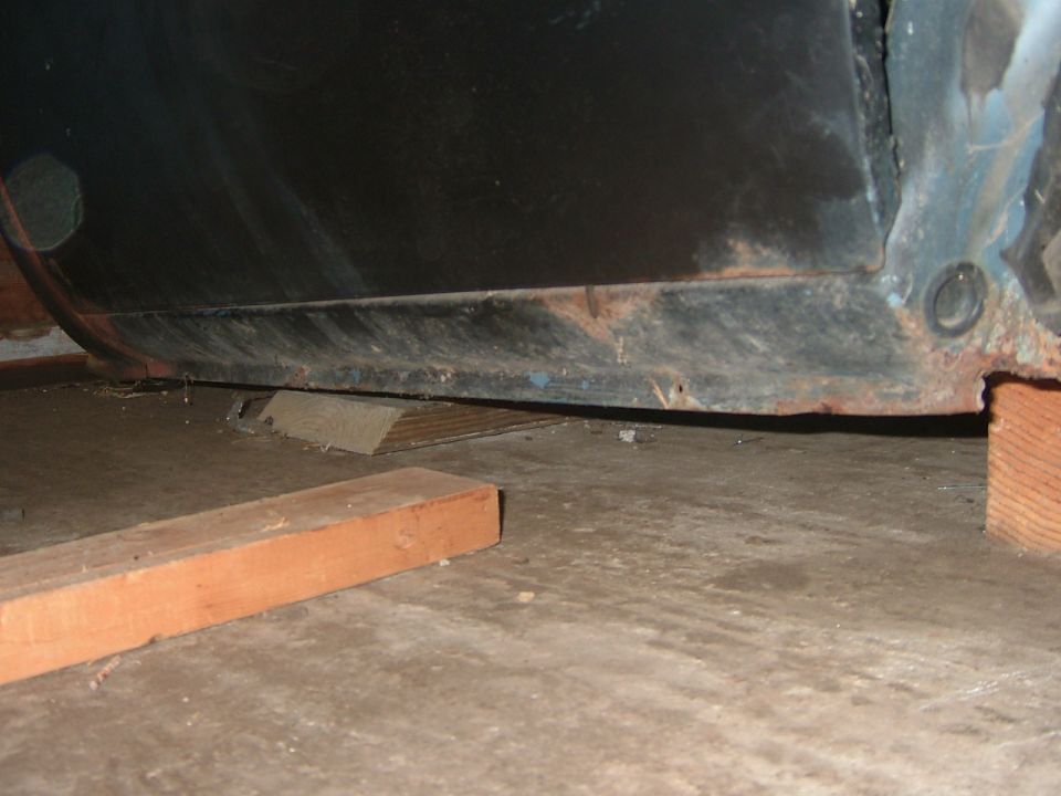 Close-up of a vehicle's lower body panel, showing rust and being supported by wooden blocks