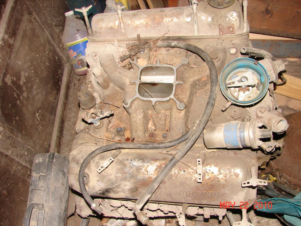 Dirty engine block with carburetor and distributor visible. A bottle of fluid is attached to the side