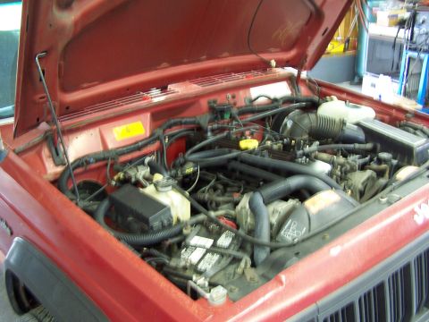 1991 Jeep Comanche - The engine bay of a red Jeep is visible with the hood raised, revealing the engine and associated parts.