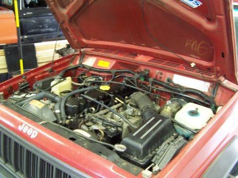 1991 Jeep Comanche - The engine bay of a red 1991 Jeep Comanche, showing the engine and various components under the open hood.