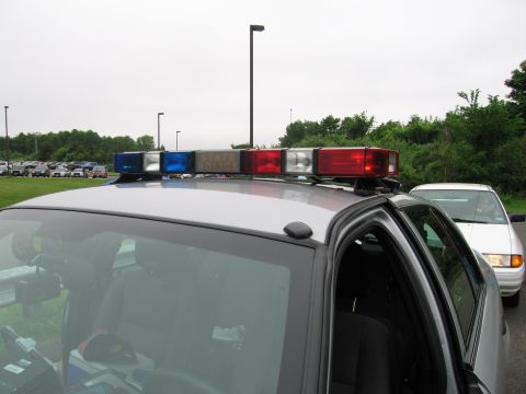 1991 Ford LTD Crown Victoria - roof-mounted police light bar with red, blue and clear lenses sits atop a gray cruiser in a parking lot under an overcast sky.