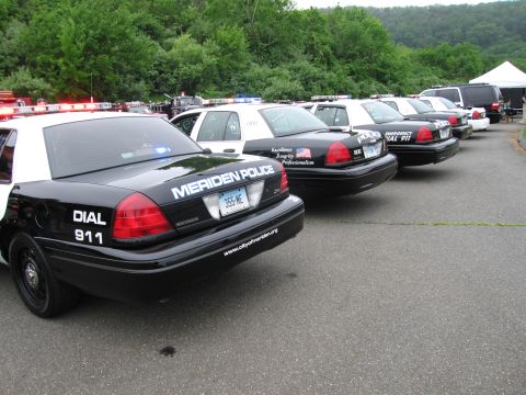 1991 Ford LTD Crown Victoria - row of black-and-white Meriden Police Ford Crown Victoria cruisers parked at an angle on pavement with trees behind at an outdoor display.