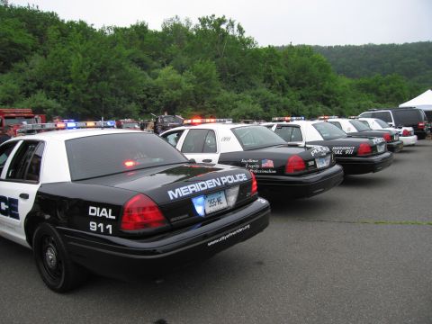 1991 Ford LTD Crown Victoria - lineup of black-and-white Meriden Police cruisers with light bars active, parked diagonally at an outdoor first-responder display.