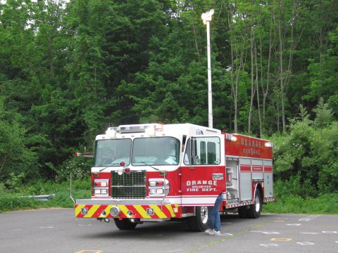 1991 Ford LTD Crown Victoria - red and white Orange Volunteer Fire Dept. rescue truck with chevron striping parked on pavement in front of a tree line.