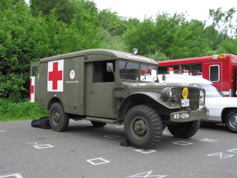 1991 Ford LTD Crown Victoria - olive-drab U.S. Army medical service ambulance truck with red cross emblems and military markings parked beside a red fire truck.