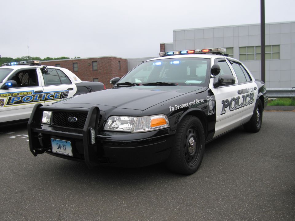 Black-and-white Police Crown Victoria with grille guard, front three-quarter