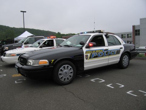 1991 Ford LTD Crown Victoria - black-and-white Town of Berlin Police Crown Victoria cruiser with blue-and-yellow door graphics, parked beside other vehicles.