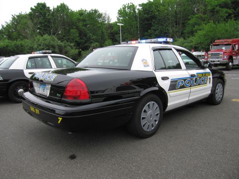 1991 Ford LTD Crown Victoria - Rear three-quarter view of a black-and-white Town of Berlin Police cruiser marked Dial 911, with a fire truck visible behind.