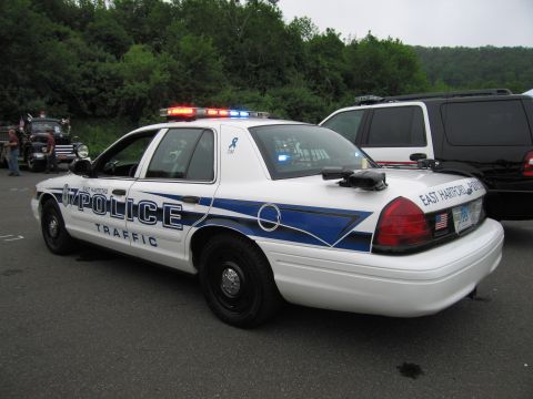 1991 Ford LTD Crown Victoria - white Ford Crown Victoria with blue graphics lettered 'East Hartford Police Traffic', parked outdoors with light bar lit.