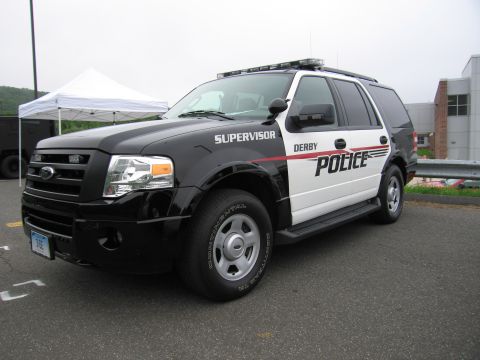 1991 Ford LTD Crown Victoria - black-and-white Ford Expedition SUV marked 'Derby Police Supervisor' parked on pavement near a tent.