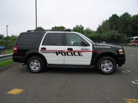 1991 Ford LTD Crown Victoria - Side profile of a black-and-white Ford Expedition lettered 'Derby Police Supervisor', parked on a road with trees behind.