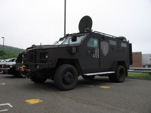 1991 Ford LTD Crown Victoria - black armored tactical police truck with turret hatch and gun ports, parked in a lot beside other vehicles.