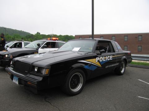 1991 Ford LTD Crown Victoria - black Buick Regal coupe lettered 'Police City of Bridgeport' with yellow and blue graphics, on display in a lot.