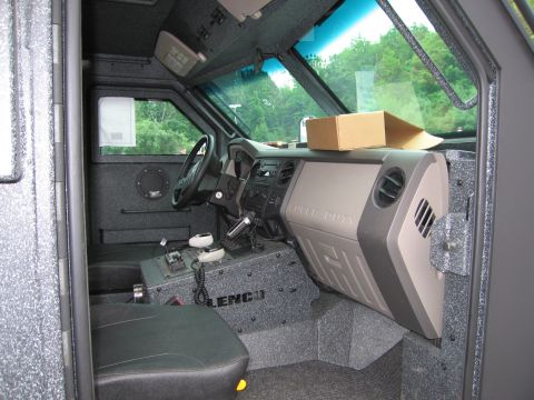 1991 Ford LTD Crown Victoria - Interior cab of an armored Lenco police truck showing the steering wheel, dashboard, padded seat and 'Lenco' console panel.
