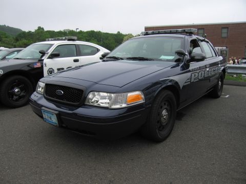 1991 Ford LTD Crown Victoria - dark blue Ford Crown Victoria police interceptor with roof light bar, parked among other cruisers outdoors.