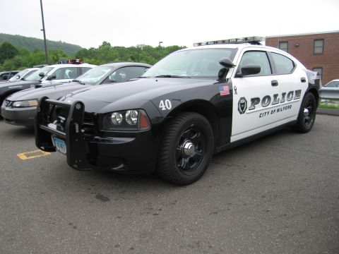 1991 Ford LTD Crown Victoria - black-and-white Dodge Charger marked 'Police City of Milford 40' with push bar, parked in a lot of cruisers.