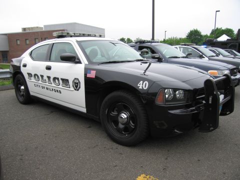 1991 Ford LTD Crown Victoria - black-and-white Dodge Charger lettered 'Police City of Milford 40' parked among other police vehicles outdoors.