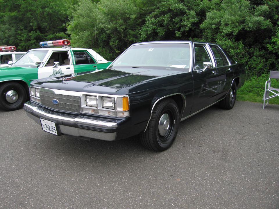 Black 1980s Ford LTD Crown Victoria police sedan parked beside a green patrol car