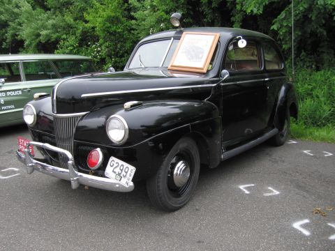 1991 Ford LTD Crown Victoria - black early-1940s Ford two-door sedan State Police car with a roof beacon and a framed placard in the windshield.