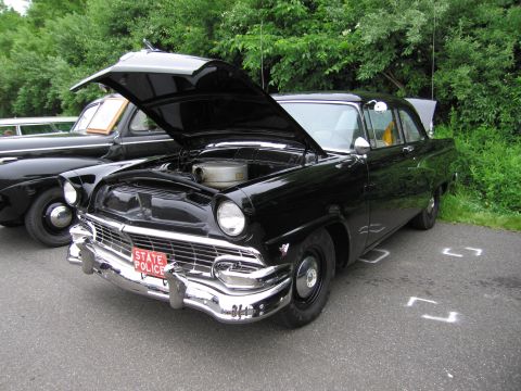 1991 Ford LTD Crown Victoria - black mid-1950s Ford sedan with its hood raised showing the engine and a red 'STATE POLICE' plate at the grille.