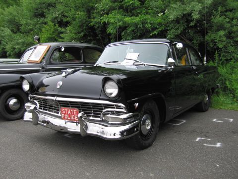 1991 Ford LTD Crown Victoria - black mid-1950s Ford two-door sedan with chrome bumpers and a red 'STATE POLICE' plate, parked at a show.