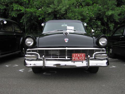 1991 Ford LTD Crown Victoria - Head-on view of a black mid-1950s Ford with dual headlights, chrome grille and bumper and a red 'STATE POLICE' plate.