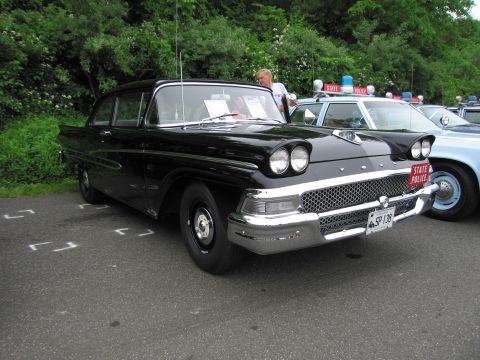 1991 Ford LTD Crown Victoria - black late-1950s Ford sedan with quad headlights and a red 'STATE POLICE' plate, other cruisers in background.