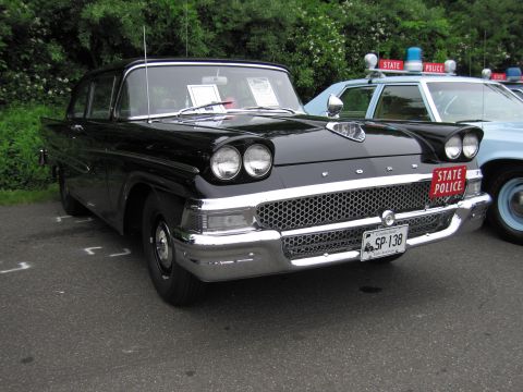 1991 Ford LTD Crown Victoria - black late-1950s Ford 'STATE POLICE' sedan with quad headlights, parked next to a light-blue dome-lit cruiser.