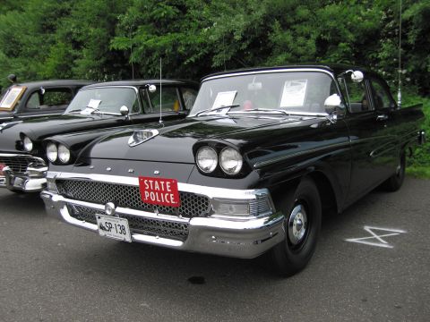 1991 Ford LTD Crown Victoria - black late-1950s Ford sedan with chrome grille and red 'STATE POLICE' plate, parked among other classic cars.