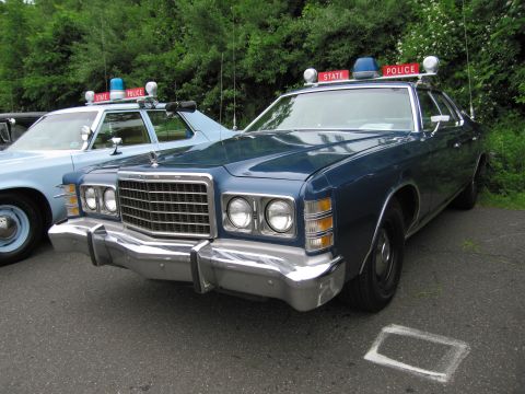 1991 Ford LTD Crown Victoria - dark-blue 1970s Ford full-size State Police sedan with stacked quad headlights and roof lights, in a cruiser row.