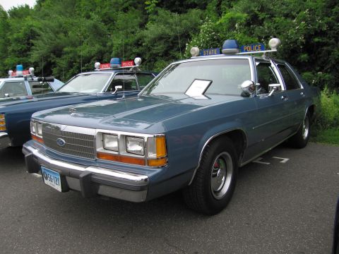 1991 Ford LTD Crown Victoria - blue 1980s Ford LTD Crown Victoria State Police sedan with roof light bar, parked in a line of cruisers.