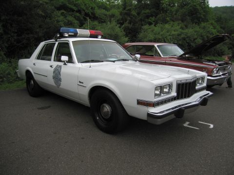 1991 Ford LTD Crown Victoria - white 1980s Dodge Diplomat police sedan with a door emblem decal and roof light bar, parked at a show.